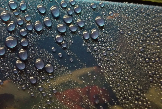 Close-up of water beading on a car's surface, showcasing the protective gloss from ceramic coating.