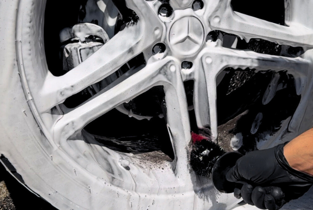 Deep cleaning a car tire with foamy soap, part of an expert car detailing service.