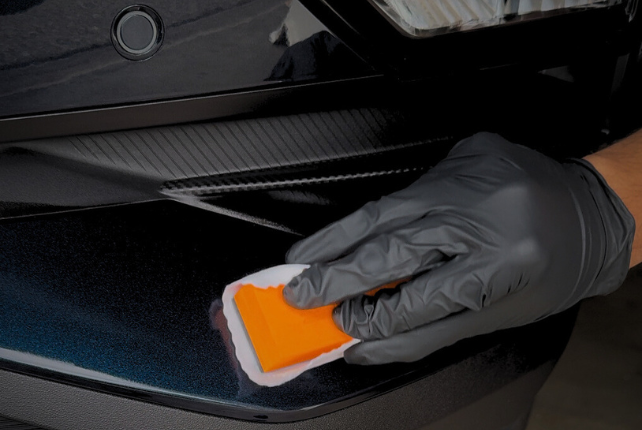 Technician carefully applying ceramic coating on a car, enhancing its protection and shine for a client’s vehicle.